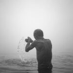 An elderly man performs a peaceful morning ritual in the sacred Ganges River, enveloped by mist.